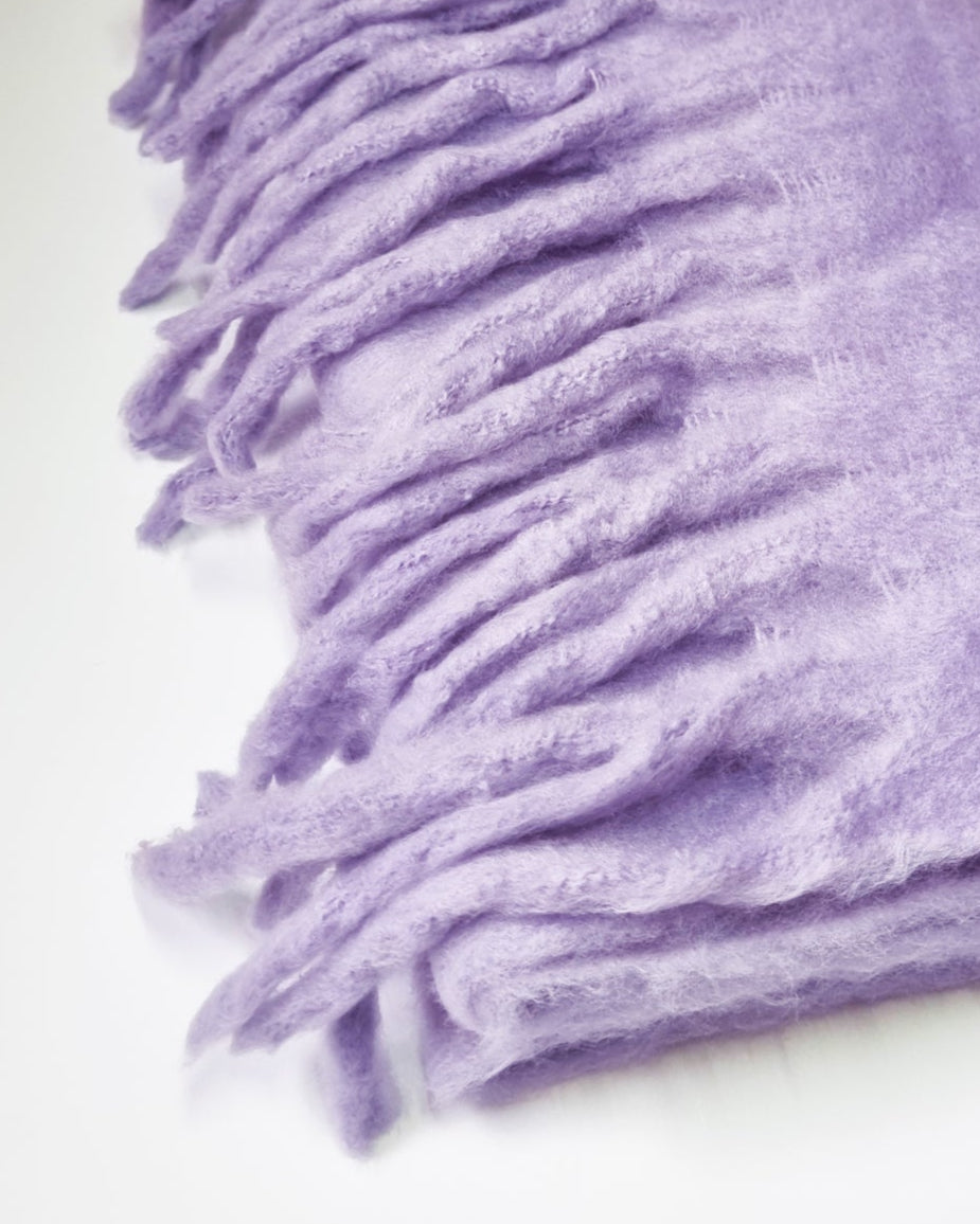 Folded purple blanket with tassels on a white background